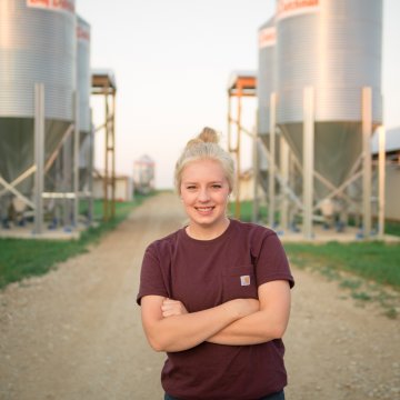 नेब्रास्का के किसान हन्ना बोर्ग अपने परिवार के खेत पर मुर्गे के खलिहान के बीच खड़े हैं